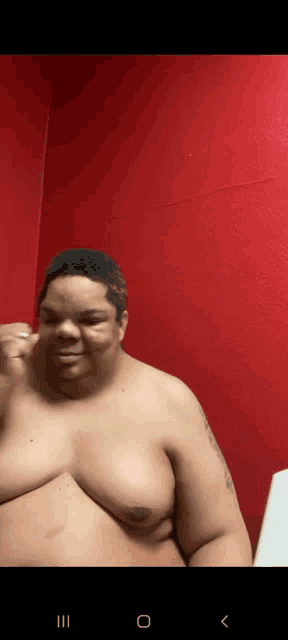 a man without a shirt is standing in front of a red wall .