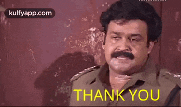 a man with a mustache is standing in front of a red wall and says thank you .