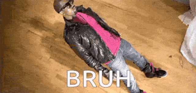 a man in a leather jacket is laying on a wooden floor with the words bruh written on the floor .