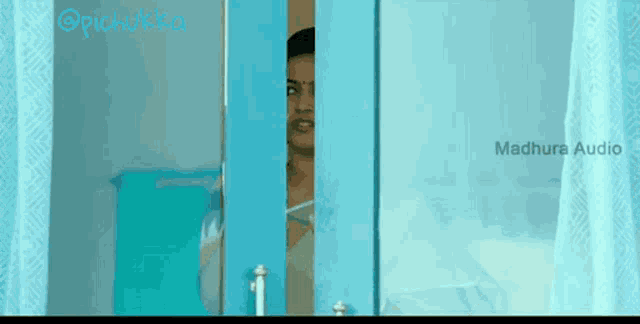 a woman is peeking out of a blue door with the words madhura audio written on it