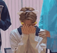 a young man wearing a cat ear headband is covering his face with his hands .