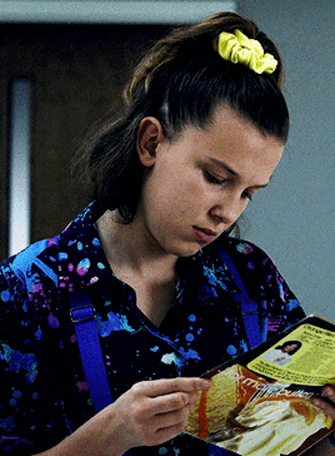 a girl with a yellow scrunchie in her hair is reading a book about french fries
