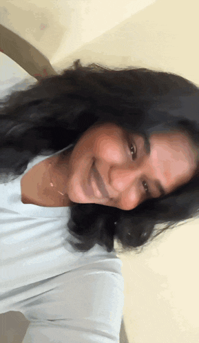 a woman with long black hair wearing a white shirt smiles for the camera