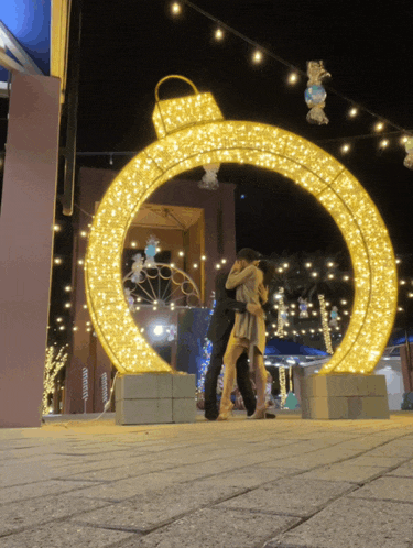a couple hugging in front of a large gold ornament