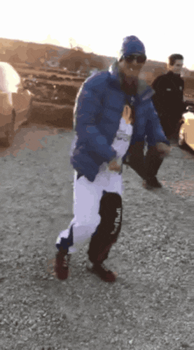 a man wearing a blue jacket and white pants is dancing in a parking lot