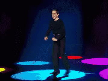 a man in a black shirt is dancing on a stage with colorful lights