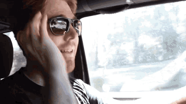 a man wearing sunglasses and a black shirt is driving a car