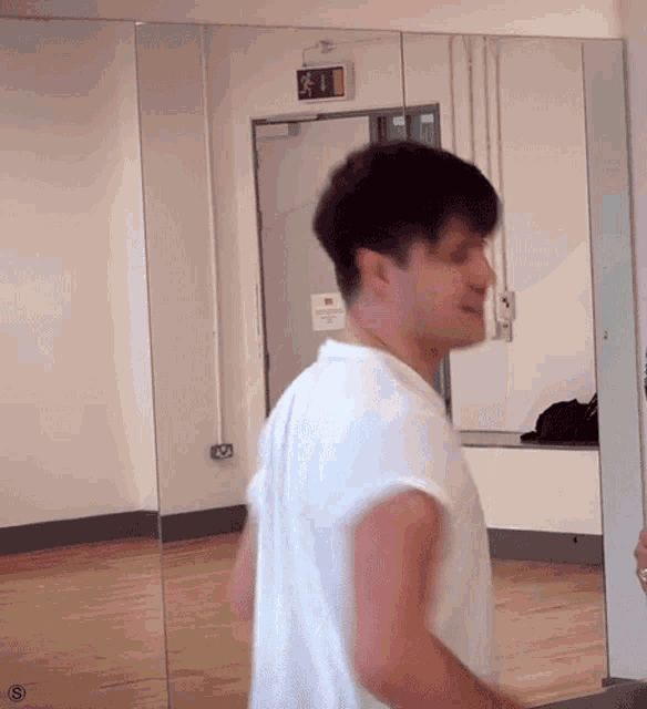 a man in a white shirt is standing in front of a mirror with an exit sign above him