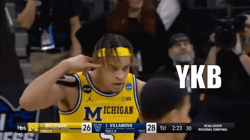 a basketball player wearing a michigan jersey holds his hand to his head