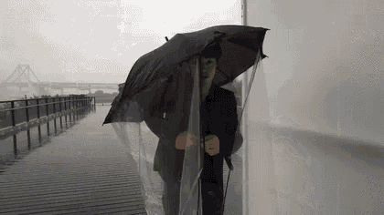 a man in a suit is holding an umbrella and covering himself with a plastic sheet .