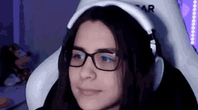 a woman wearing glasses and headphones sits in a white chair