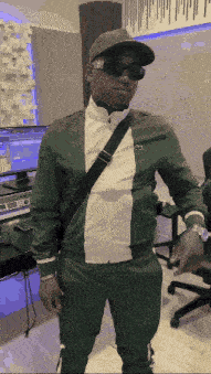 a man wearing a hat and sunglasses stands in front of a computer