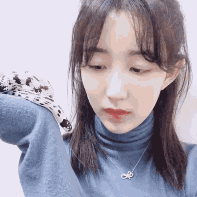 a woman wearing a blue turtleneck sweater and a necklace with a bow on it