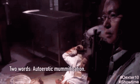 a man wearing glasses is looking at a dead body and says two words autoerotic mummification