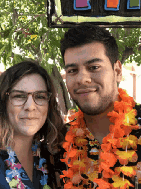 a man and a woman are posing for a picture in front of a sign that says aloha