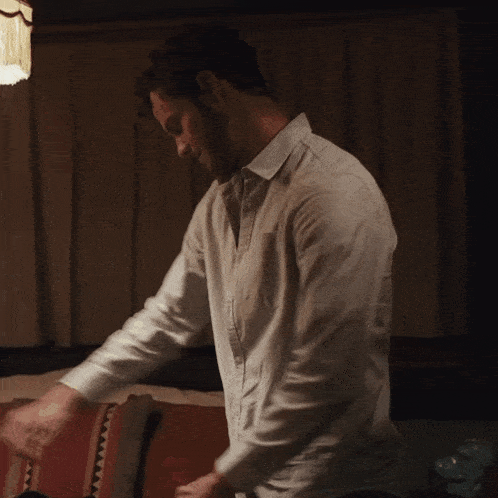 a man in a white shirt is standing next to a couch in a dark room
