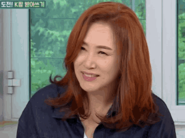 a woman with red hair is smiling in front of a window with foreign writing on it