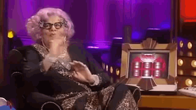 a woman with pink hair and glasses is sitting in a chair in front of a box .