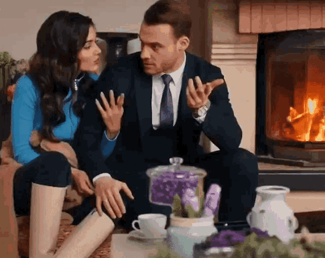 a man and a woman are sitting in front of a fireplace talking to each other