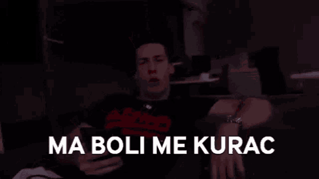 a man is flexing his muscles in a dark room with the words ma boli me kurac written on the screen .