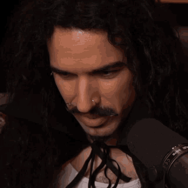 a man with long hair and a nose ring stands in front of a microphone that says ' rode ' on the bottom