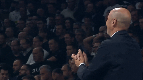 a bald man in a suit and white shirt is raising his hands in the air