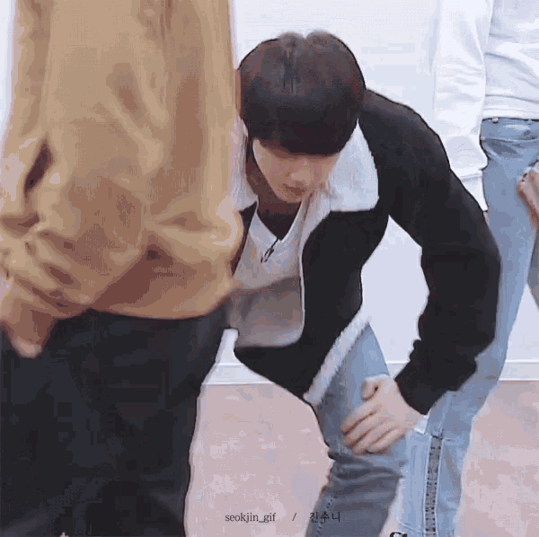 a young man is kneeling down with his hands on his knees while standing next to a group of people .