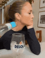 a woman is sitting at a table with a bottle of water and a glass that says deloli