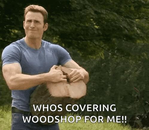 a man in a blue shirt is holding a large piece of wood and says whos covering woodshop for me !