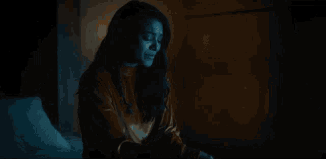 a woman is sitting on a couch in a dark room with a lamp in the background .