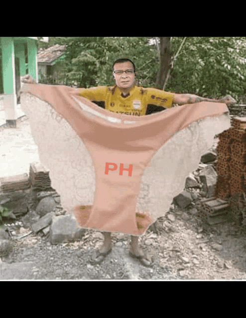 a man in a yellow shirt is holding a large pink underwear with the word ph on it
