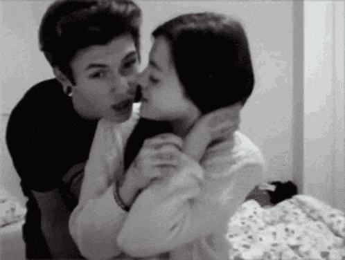 a boy and a girl are kissing in a black and white photo .