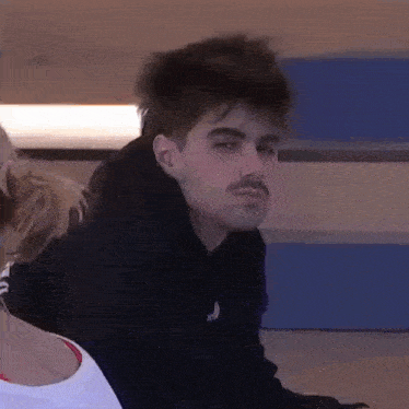 a young man with a mustache is sitting next to a woman and looking at the camera .