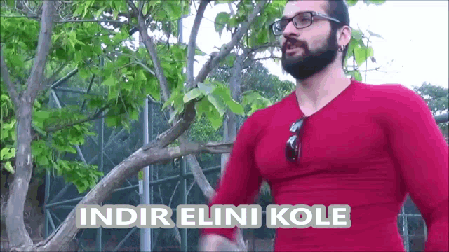 a man with a beard and glasses is wearing a red shirt that says ' indir elini kole '