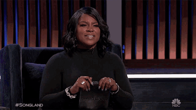 a woman sitting in front of a screen that says songland on it