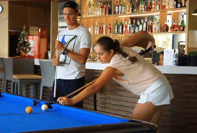 a man and a woman play pool in front of a coca cola cooler