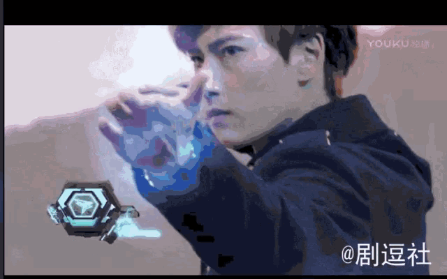 a man in a black hoodie is holding a glowing object in his hand with chinese writing on the bottom right corner