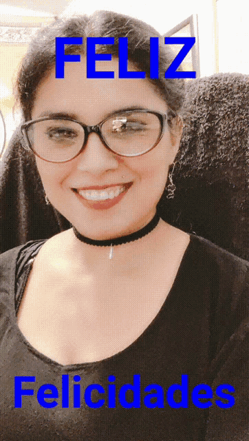 a woman with glasses and a choker smiles in front of a sign that says feliz