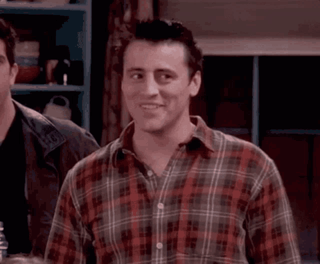a man in a plaid shirt is smiling while standing next to another man in a kitchen .