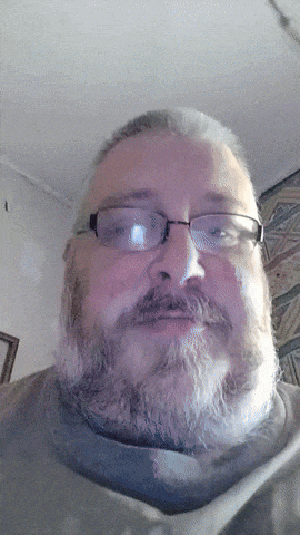 a man with a beard wearing glasses and a grey shirt