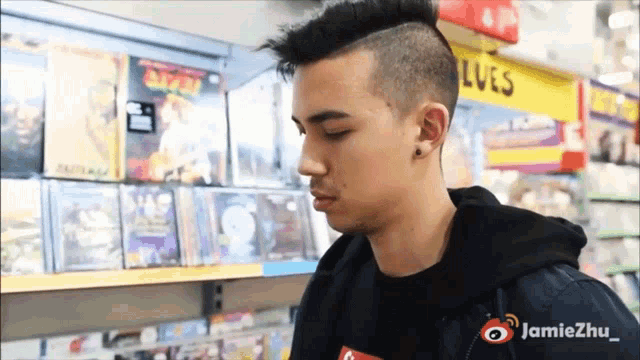 a man with a mohawk stands in front of a shelf with lues on it