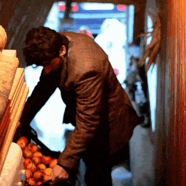 a man in a brown jacket is reaching into a container of apples