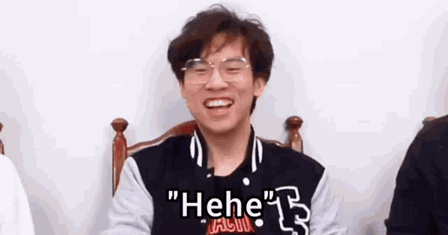 a man wearing glasses is sitting in a chair and laughing with the words " he he " written on the bottom .