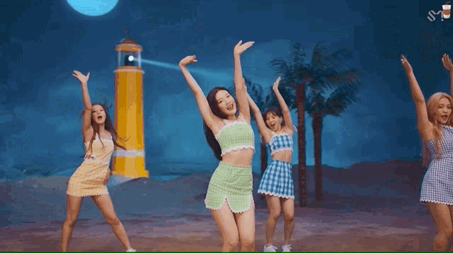 a group of women are dancing on a beach in front of a lighthouse