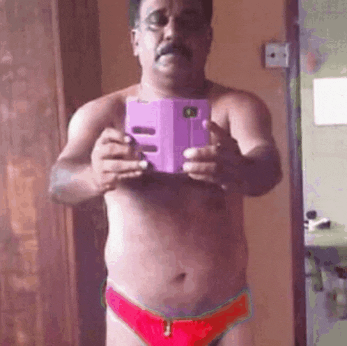 a shirtless man in red underwear is taking a selfie with a purple cell phone .