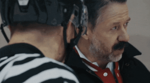 a man with a beard wearing a helmet talks to a referee