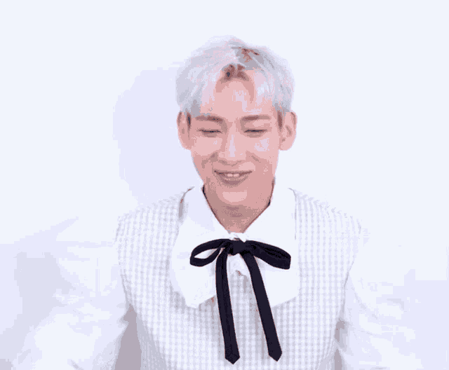 a young man wearing a white shirt with a black tie making a heart shape with his hands