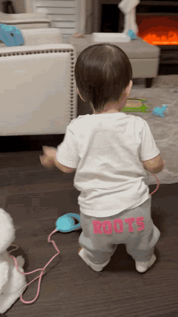 a baby wearing a white shirt and grey pants with the word roots on the back