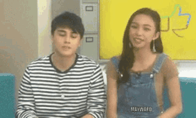 a man and a woman are sitting next to each other on a couch in front of a yellow wall .