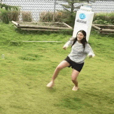 a woman is dancing on the grass in front of a sign that says ' thailand ' on it .